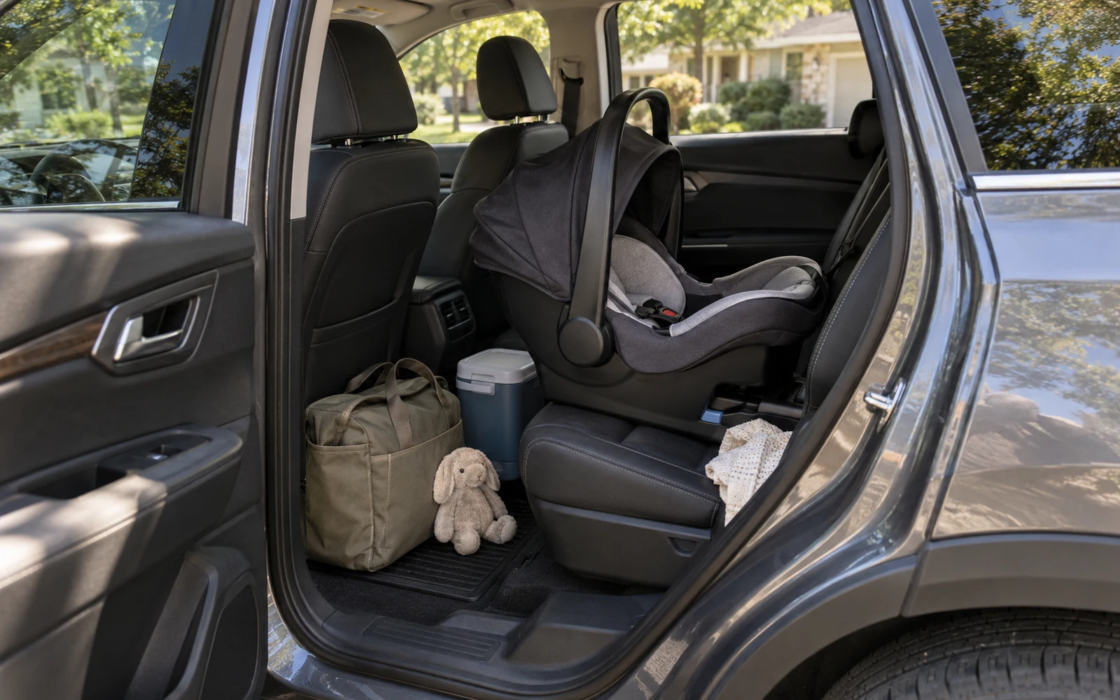 The open rear door of an unbadged family SUV showing an empty rear-facing child seat, a diaper bag and a small cooler packed for a road trip